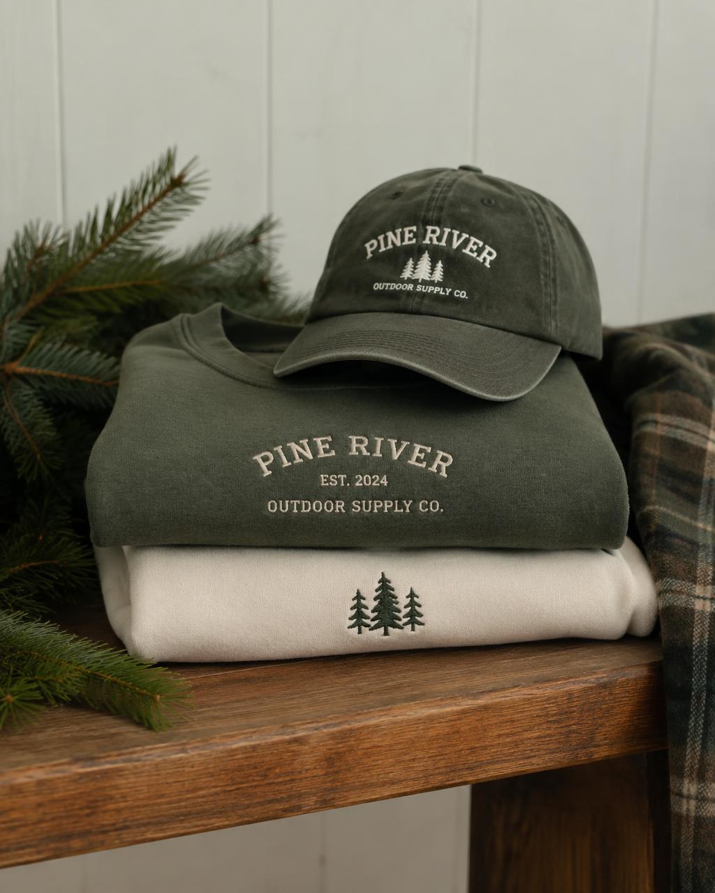 Folded evergreen and cream embroidered sweatshirts with a cap on a wooden bench